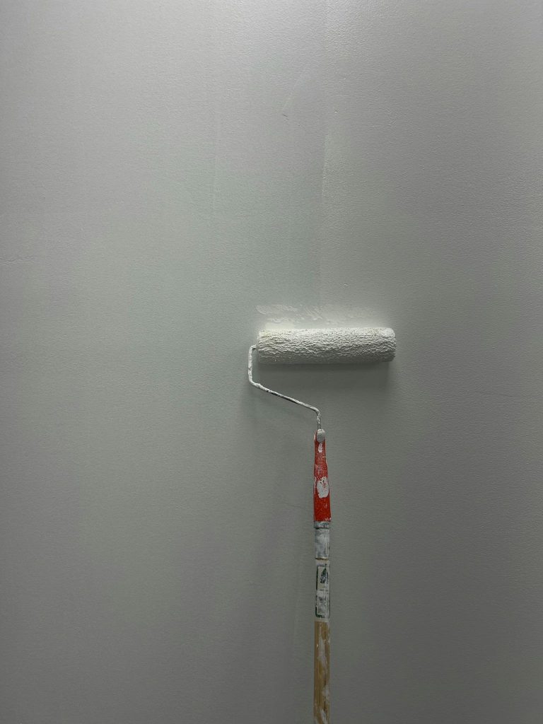 Close-up of a paint roller applying light gray paint to a wall. Simple and clean.