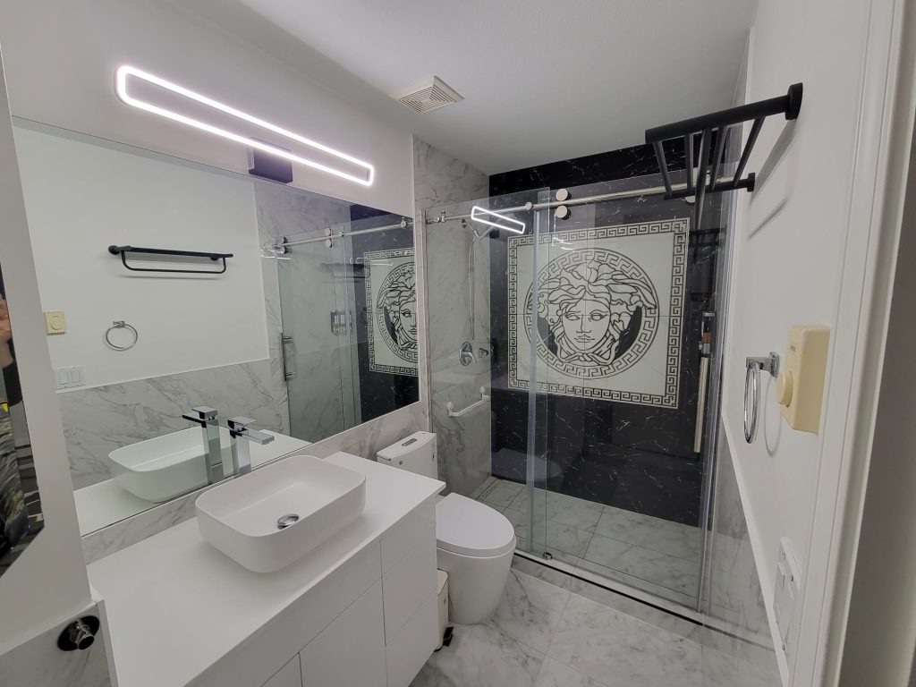 Freshly painted luxury bathroom with crisp white walls, modern vanity, marble-look finishes, frameless glass shower, and striking black feature tile.