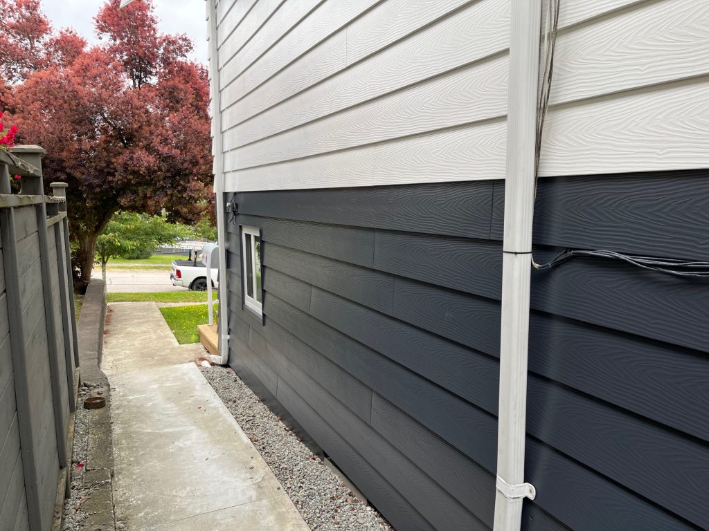 Exterior siding painting project in Port Moody featuring white upper siding, dark charcoal lower siding, and clean professional finish along side yard