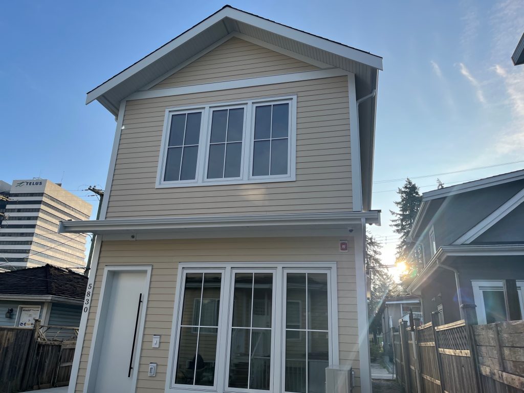 Front view of a freshly painted two-storey house with light beige siding, bright white trim, and large front windows under a clear blue sky. Another title option for a more premium feel: Clean Exterior Repaint with Modern Contrast Trim