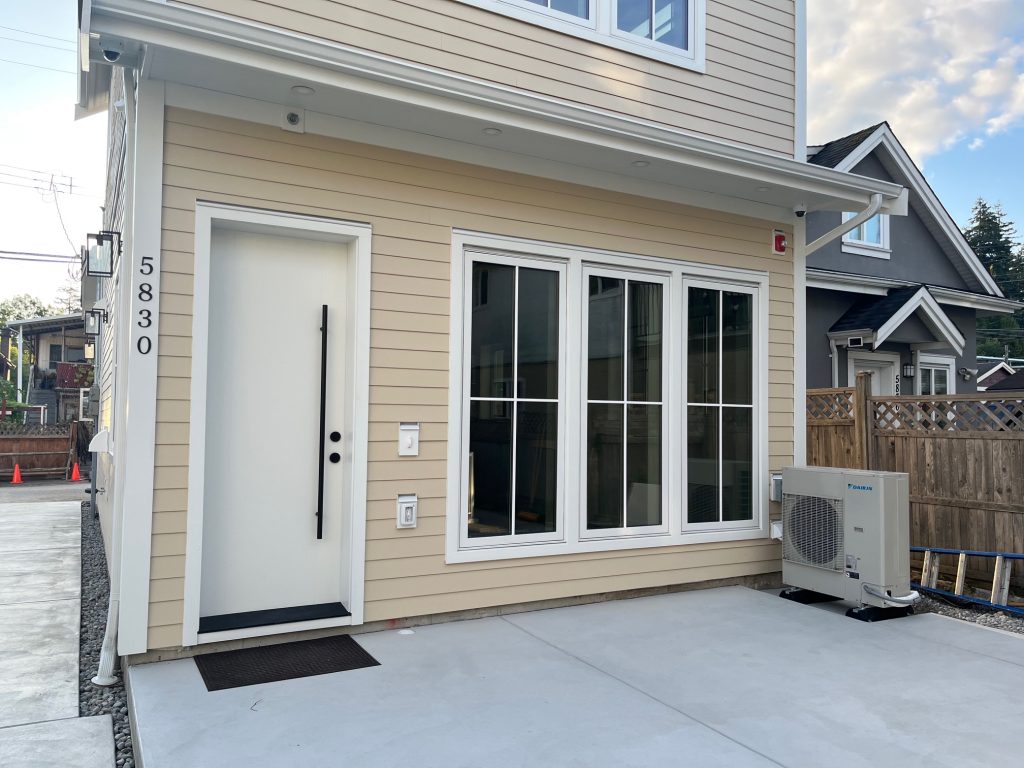 Close-up front view of a freshly painted modern home exterior with warm beige siding, crisp white trim, a white entry door, and large black-framed windows. Another good title option: Premium Exterior Repaint with Clean White Trim and Neutral Tones