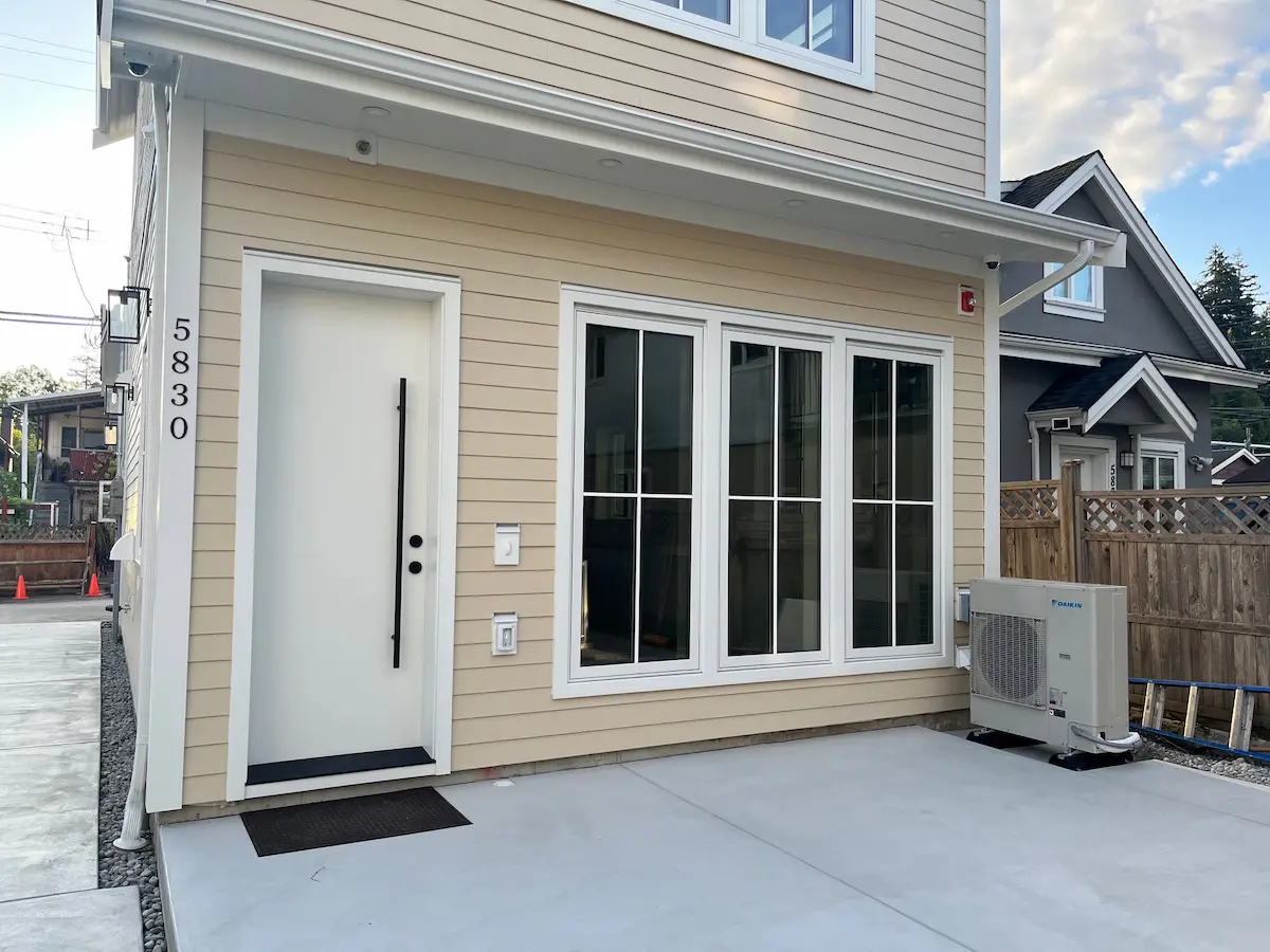 Close-up front view of a freshly painted modern home exterior with warm beige siding, crisp white trim, a white entry door, and large black-framed windows. Another good title option: Premium Exterior Repaint with Clean White Trim and Neutral Tones