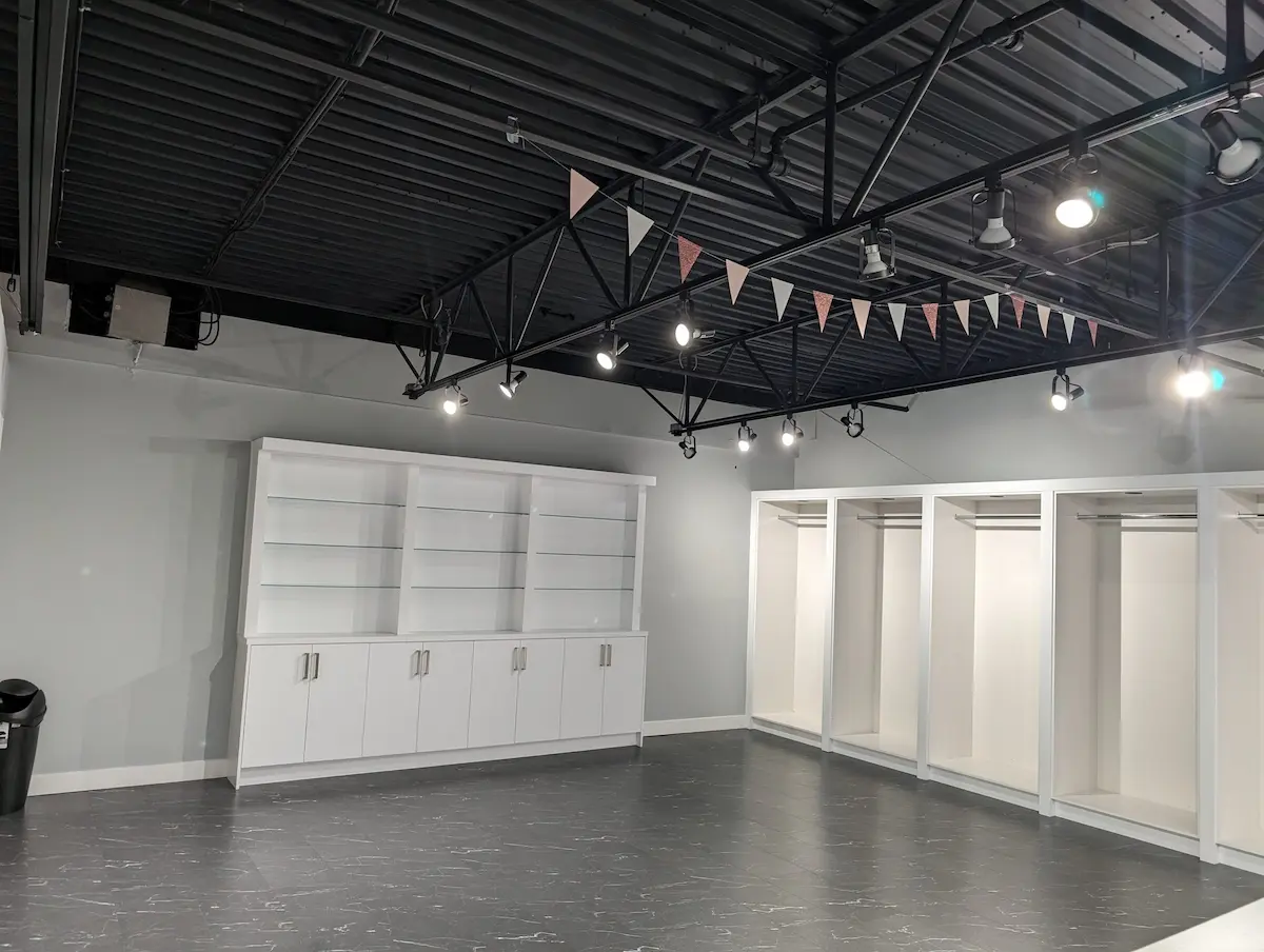 Freshly painted retail interior with light gray walls, white built-in display shelving, open merchandise bays, black exposed ceiling, and track lighting.